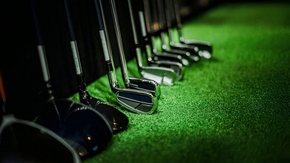 Golf clubs on the turf inside an Endless 18 simulator bay
